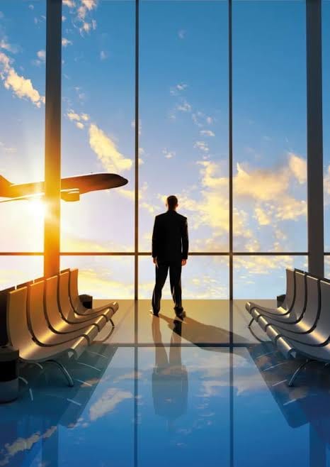 Traveller at an airport window watching a plane take off at sunset